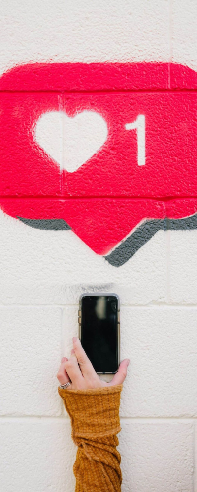 Une personne tenant un téléphone devant un mur de likes, illustrant l'importance de l'engagement sur les réseaux sociaux.Photo de Karsten Winegeart sur Unsplash