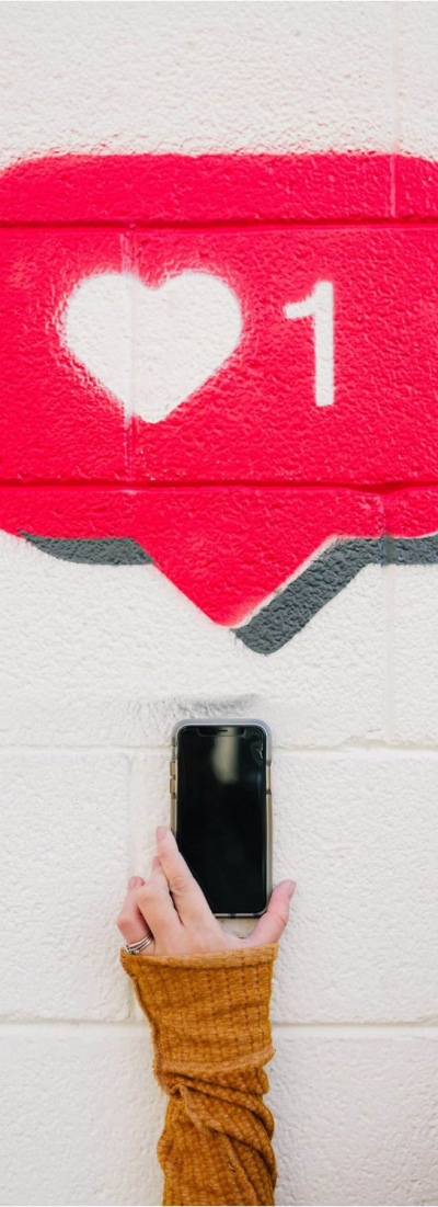 Une personne tenant un téléphone devant un mur de likes, illustrant l'importance de l'engagement sur les réseaux sociaux.Photo de Karsten Winegeart sur Unsplash